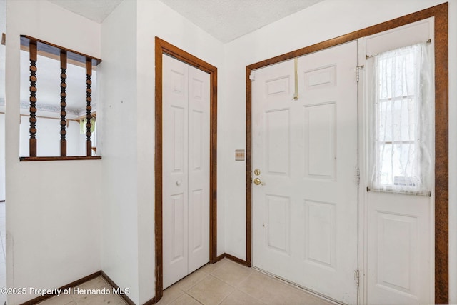 foyer featuring a textured ceiling, baseboards, and light tile patterned floors