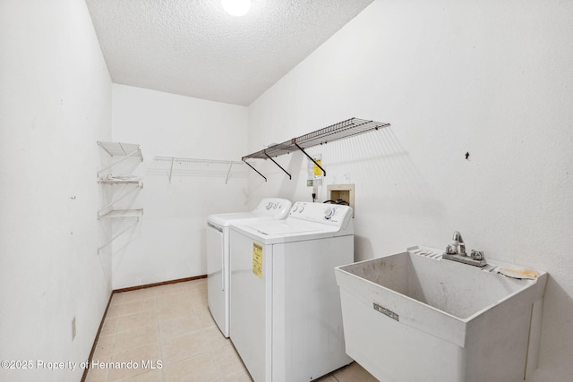 laundry room featuring laundry area, baseboards, a textured ceiling, washing machine and dryer, and a sink