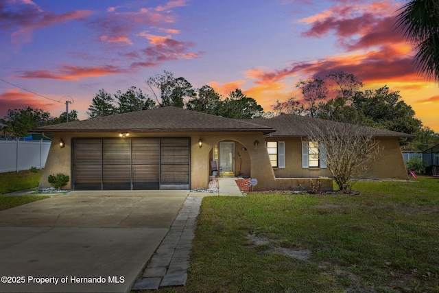 view of front of property with driveway, an attached garage, fence, a front lawn, and stucco siding