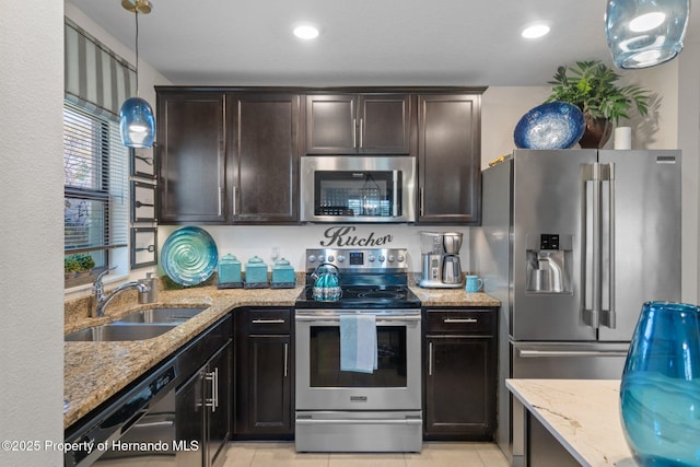 kitchen featuring dark brown cabinetry, light tile patterned floors, appliances with stainless steel finishes, light stone counters, and a sink