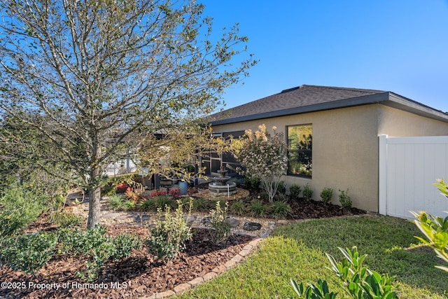 exterior space with roof with shingles, fence, a lawn, and stucco siding