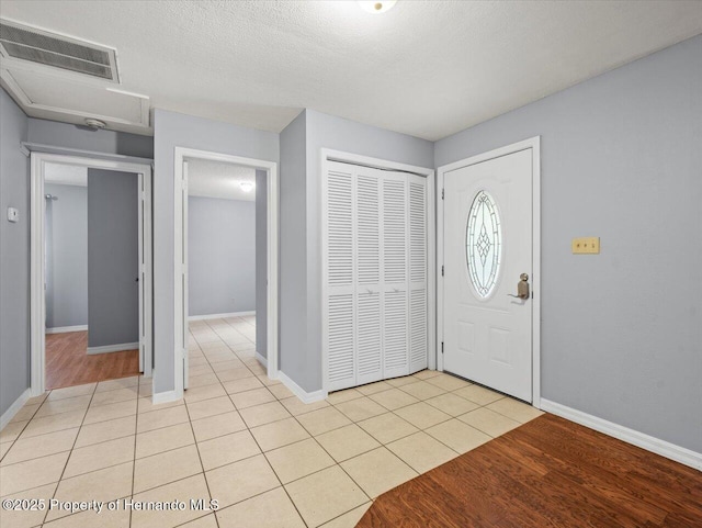 entrance foyer featuring a textured ceiling, light tile patterned flooring, visible vents, and baseboards