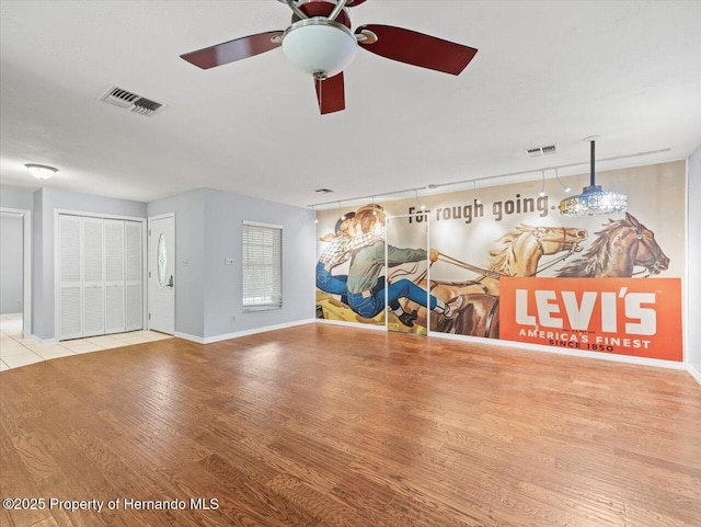 interior space featuring a ceiling fan, visible vents, baseboards, and wood finished floors