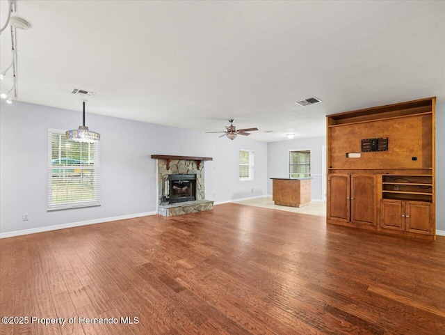 unfurnished living room with ceiling fan, visible vents, wood finished floors, and a stone fireplace