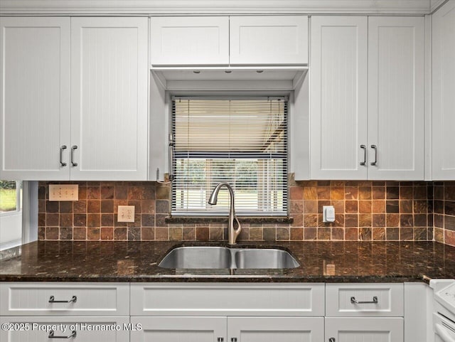 kitchen with dark stone counters, tasteful backsplash, a sink, and white cabinetry