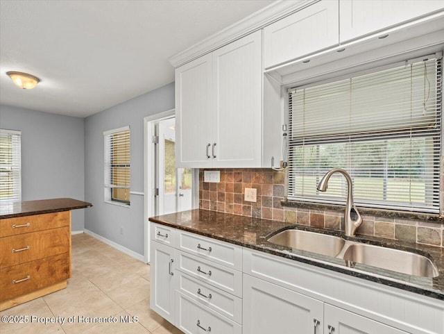 kitchen featuring light tile patterned flooring, a sink, white cabinetry, dark stone counters, and tasteful backsplash