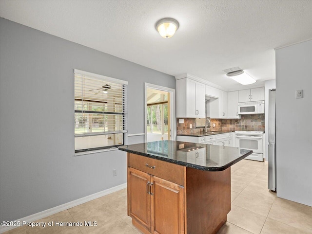 kitchen featuring tasteful backsplash, white cabinets, a sink, dark stone counters, and white appliances