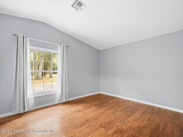 spare room featuring vaulted ceiling, wood finished floors, visible vents, and baseboards