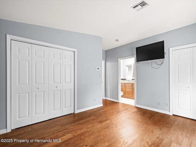 unfurnished bedroom with ensuite bathroom, wood finished floors, visible vents, baseboards, and vaulted ceiling