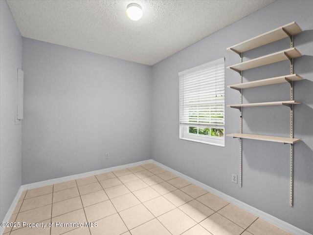 empty room with tile patterned flooring, a textured ceiling, and baseboards