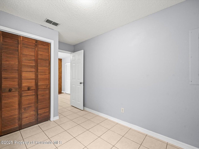 unfurnished bedroom with light tile patterned floors, a closet, visible vents, a textured ceiling, and baseboards