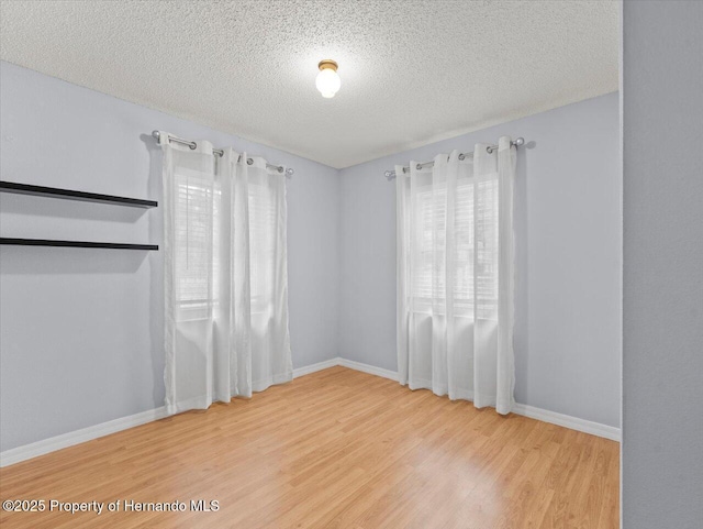 spare room with a textured ceiling, baseboards, and wood finished floors