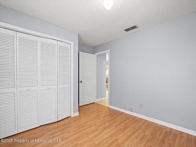 unfurnished bedroom with baseboards, visible vents, a textured ceiling, light wood-type flooring, and a closet