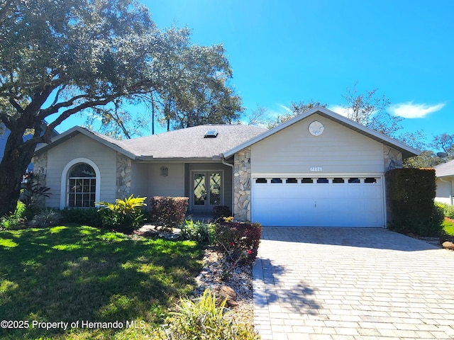 single story home with decorative driveway, a shingled roof, an attached garage, a front yard, and stone siding