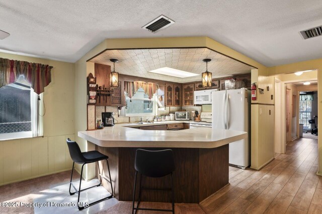 kitchen featuring glass insert cabinets, white appliances, visible vents, and a peninsula