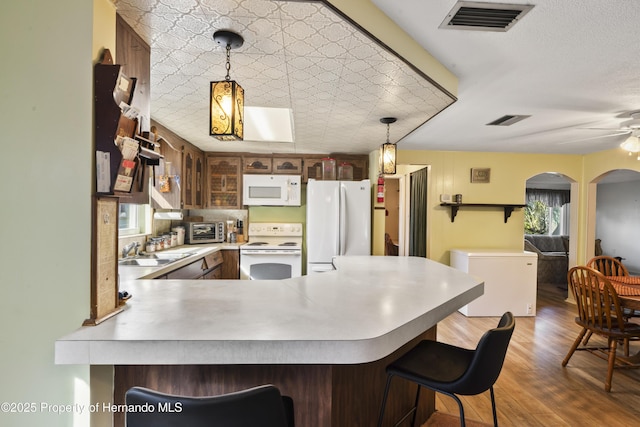 kitchen with a peninsula, white appliances, visible vents, and a sink