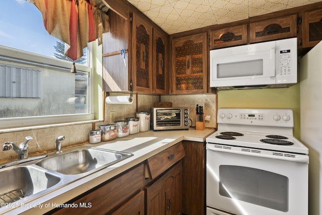 kitchen featuring a toaster, tasteful backsplash, light countertops, a sink, and white appliances