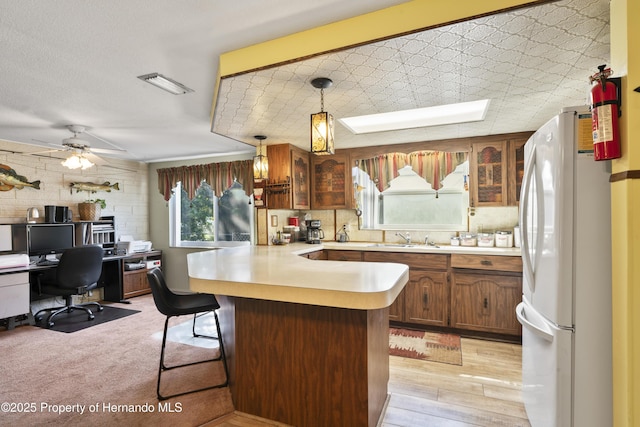 kitchen with a peninsula, a sink, a kitchen breakfast bar, light countertops, and freestanding refrigerator