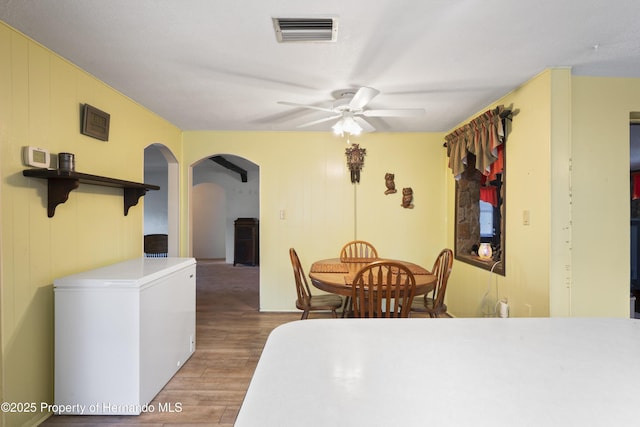 dining space featuring ceiling fan, visible vents, arched walkways, and wood finished floors