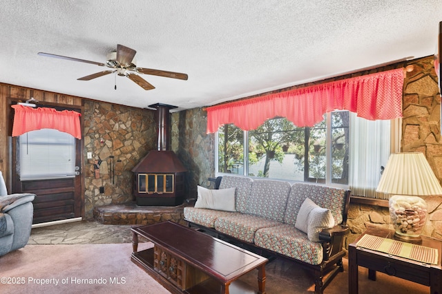 carpeted living room featuring a ceiling fan, a wood stove, and a textured ceiling