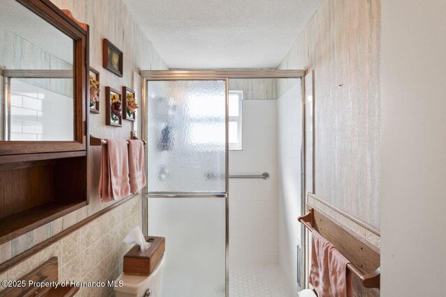 full bathroom with a shower stall, tile walls, and a textured ceiling