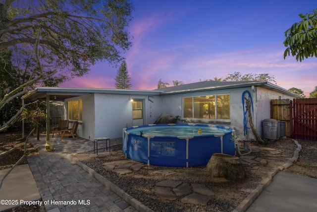 back of property at dusk with a patio area, fence, a fenced in pool, and stucco siding