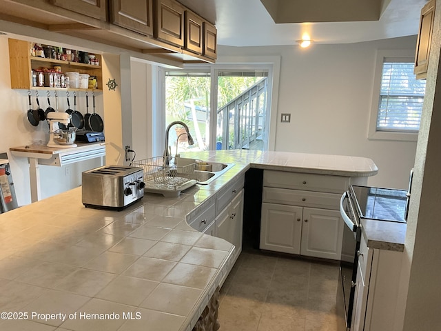 kitchen with a sink, a wealth of natural light, tile counters, and electric stove