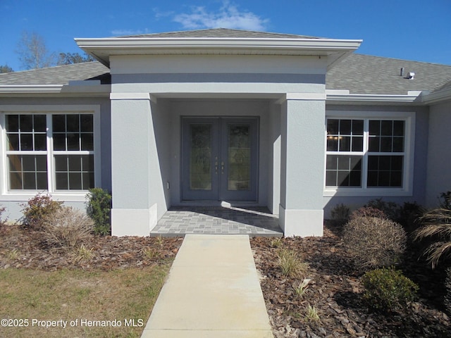 view of exterior entry featuring a shingled roof, french doors, and stucco siding