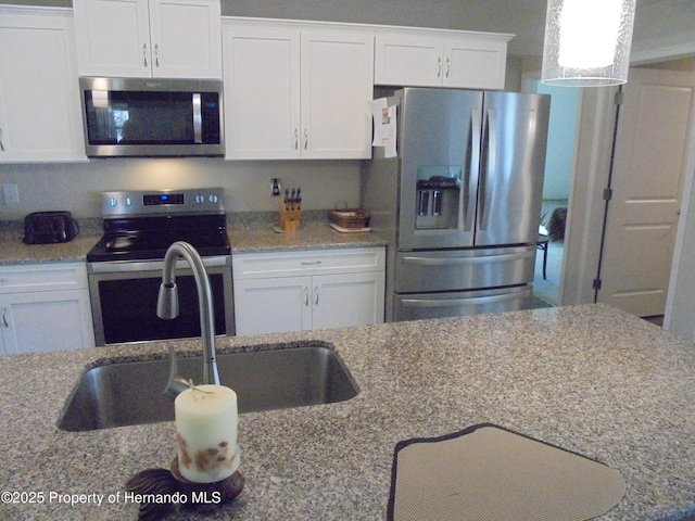 kitchen with appliances with stainless steel finishes, a sink, light stone countertops, and white cabinets