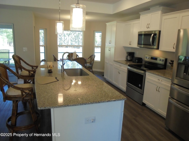 kitchen with a breakfast bar area, a kitchen island with sink, a sink, white cabinetry, and appliances with stainless steel finishes