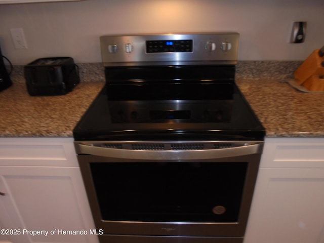 kitchen with light stone countertops, stainless steel range with electric cooktop, and white cabinetry