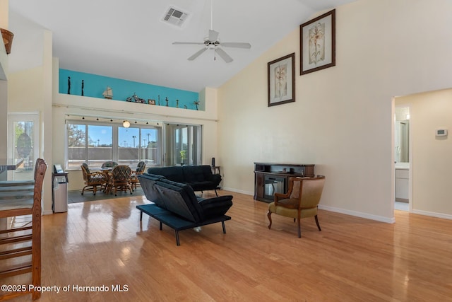 living area with high vaulted ceiling, visible vents, light wood-style flooring, and baseboards