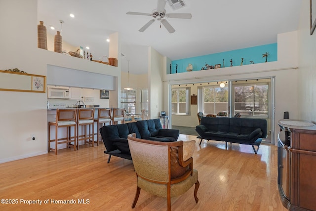 living area featuring visible vents, baseboards, a towering ceiling, ceiling fan, and light wood-type flooring