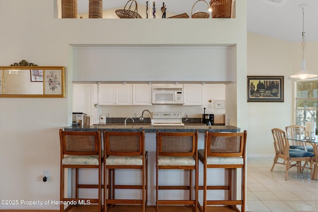 kitchen with pendant lighting, white microwave, white cabinets, range, and a kitchen breakfast bar