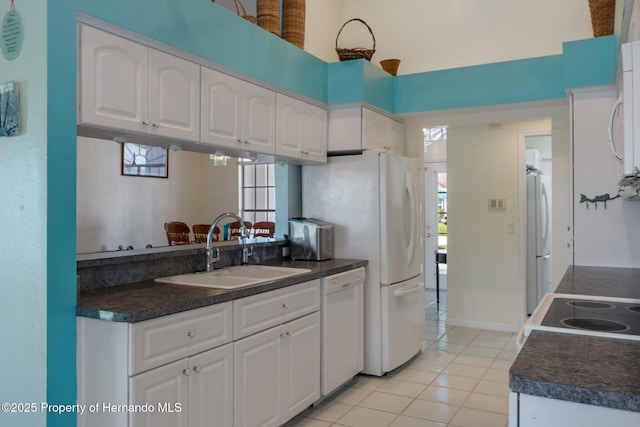 kitchen featuring dark countertops, white appliances, white cabinetry, and a sink