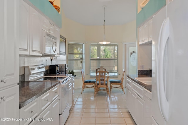 kitchen with light tile patterned floors, hanging light fixtures, white cabinets, a sink, and white appliances