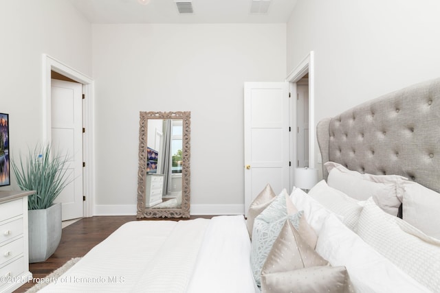 bedroom with visible vents, a towering ceiling, baseboards, and wood finished floors