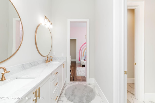 full bath with marble finish floor, double vanity, a sink, and baseboards