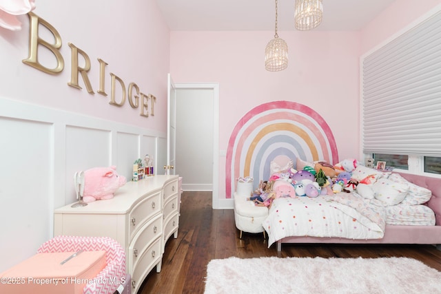 bedroom featuring an inviting chandelier, a decorative wall, dark wood finished floors, and wainscoting