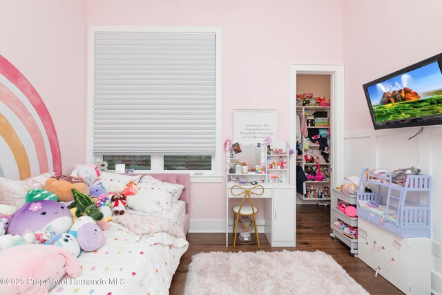 bedroom with a closet, a decorative wall, a spacious closet, and wood finished floors