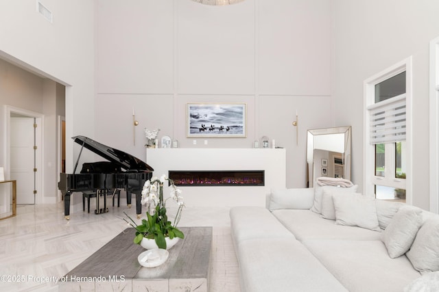 living area featuring visible vents, a glass covered fireplace, and a towering ceiling