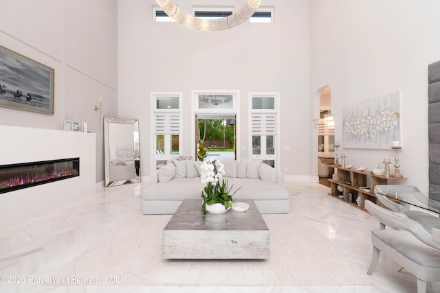 living area with arched walkways, a glass covered fireplace, and a towering ceiling