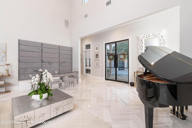 living area with a towering ceiling, visible vents, and baseboards