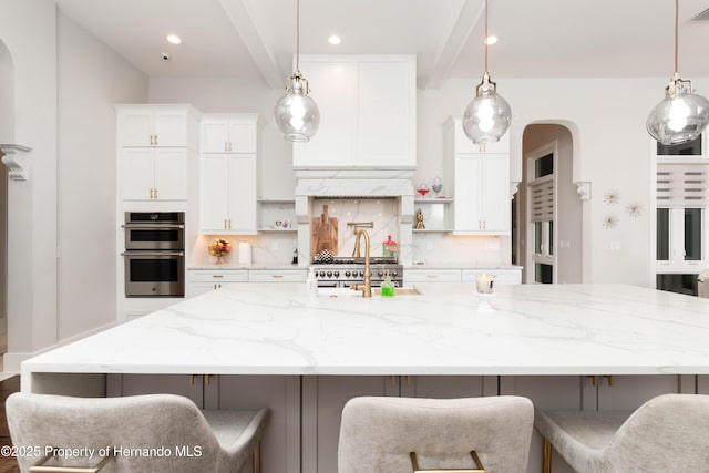 kitchen with beam ceiling, a large island, backsplash, double oven, and white cabinets