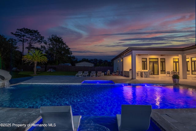 pool at dusk with a water slide, a patio area, fence, and a fenced in pool