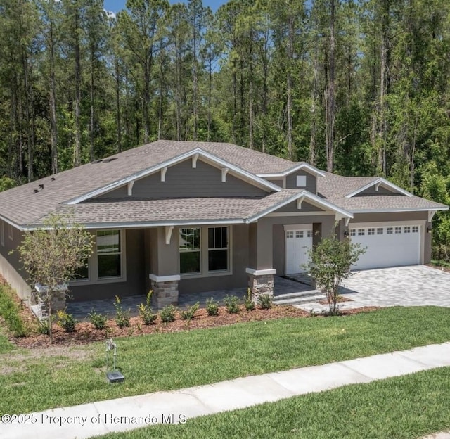 craftsman inspired home with an attached garage, stone siding, a front lawn, and roof with shingles