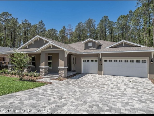 craftsman-style house featuring a garage, stone siding, decorative driveway, roof with shingles, and stucco siding