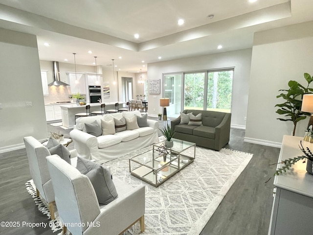 living room with dark wood-type flooring, recessed lighting, a tray ceiling, and baseboards