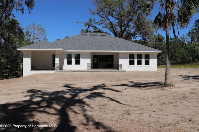back of house featuring stucco siding and a shingled roof