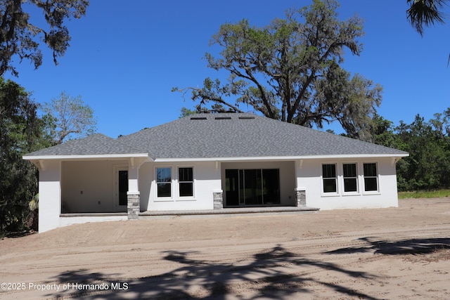 back of house with stucco siding and a shingled roof